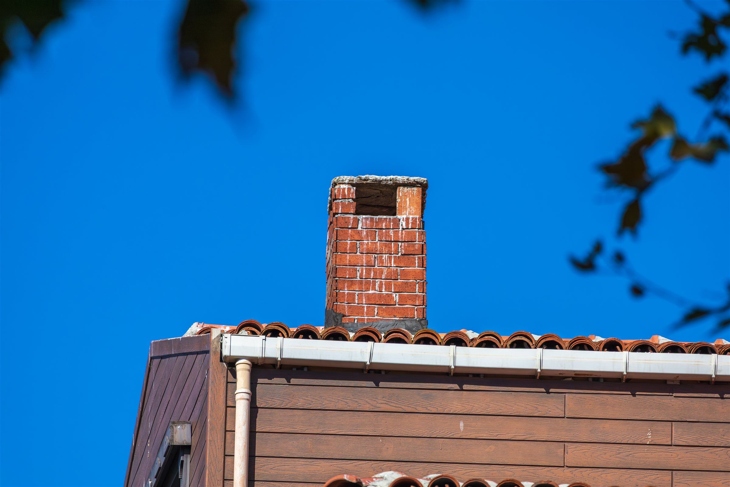 Brick chimney above a roof against a clear blue sky