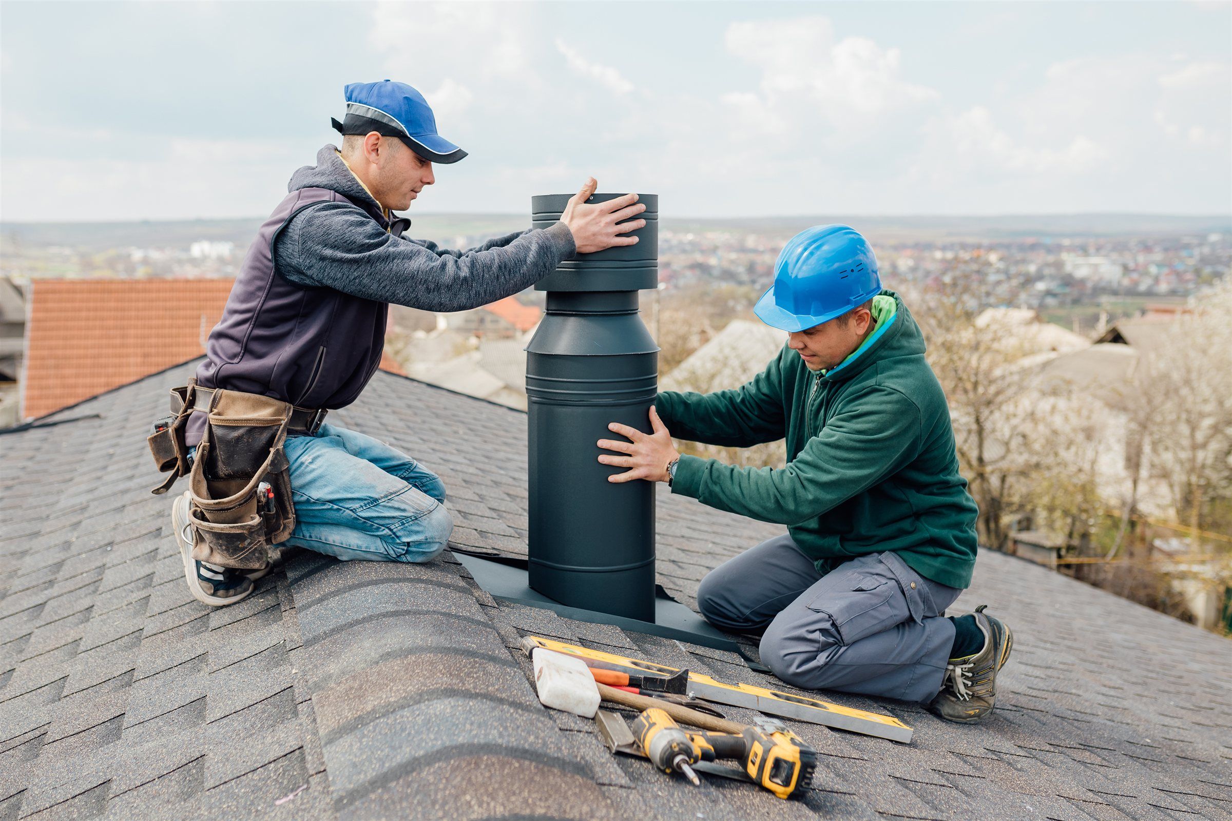 Two workers installing a new chimney section on a shingle roof