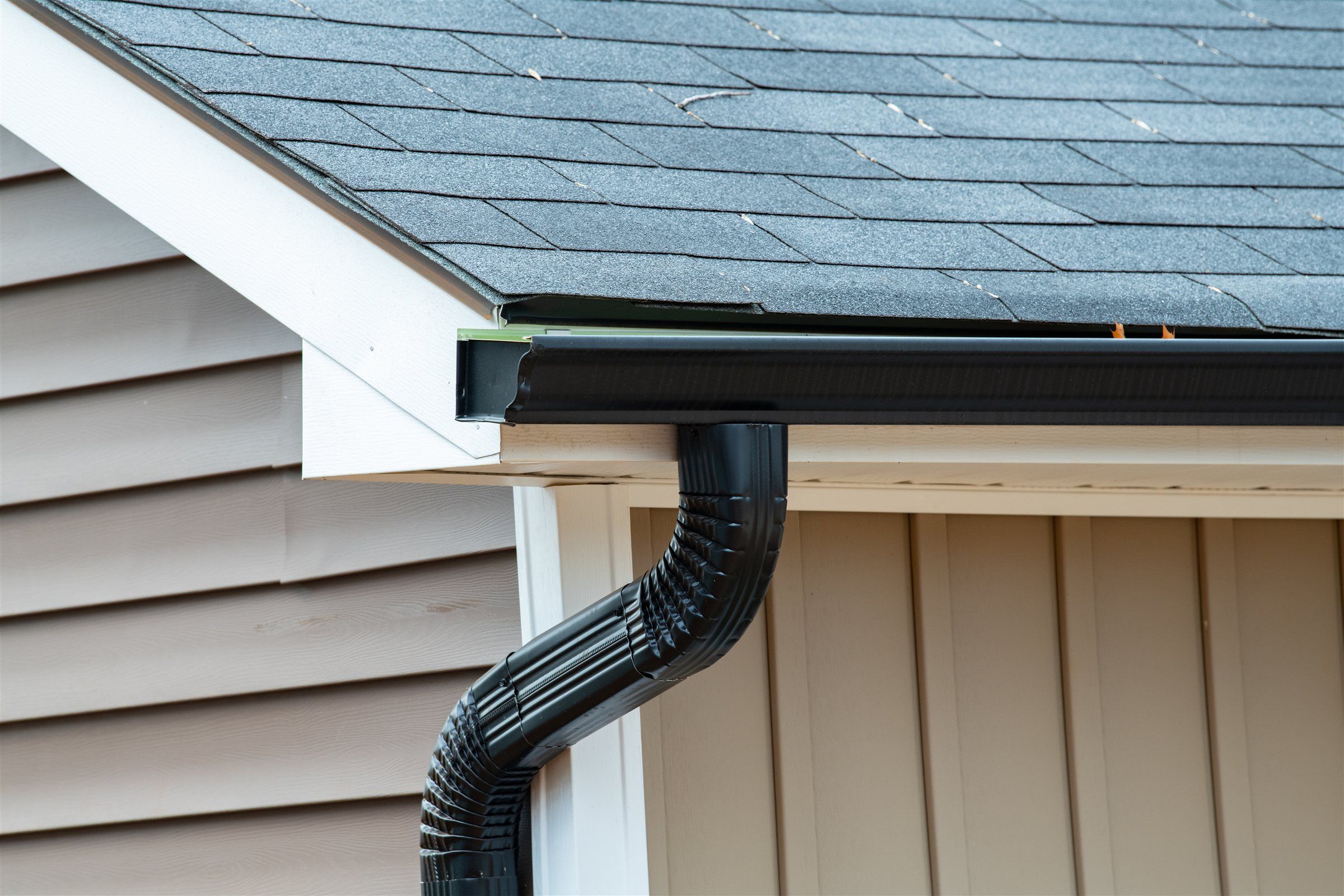 Black gutter and downspout under a shingle roof edge