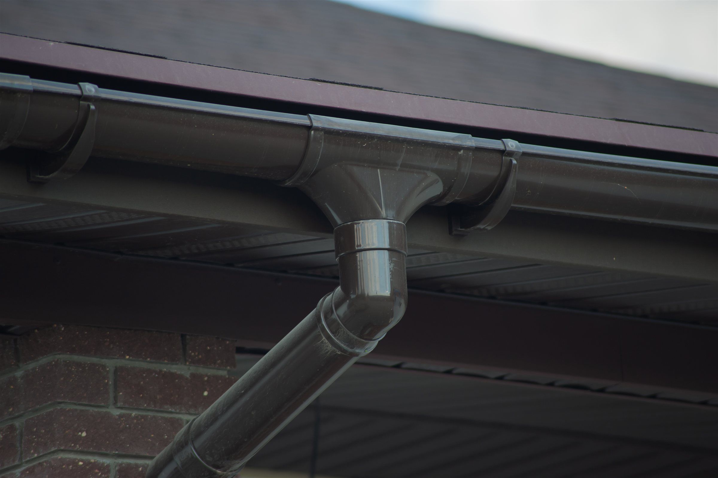 Close view of a gutter joint and downspout outlet under a roof edge