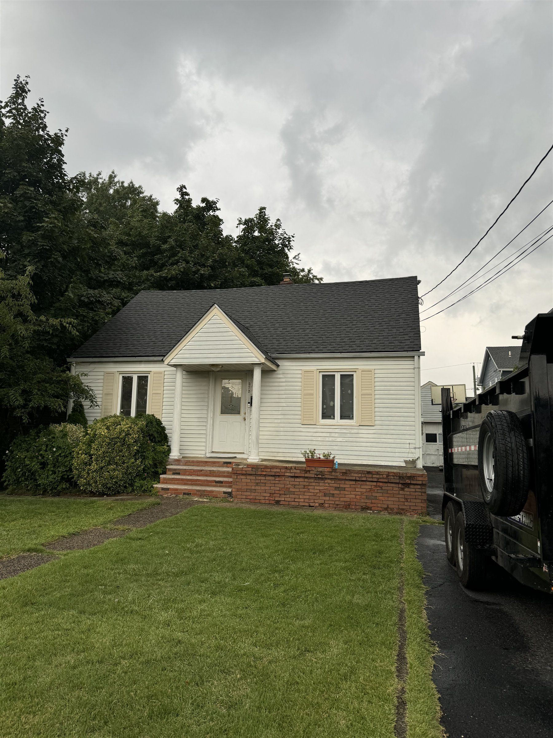 White Cape Cod home with a new dark shingle roof by ADZ Roofing